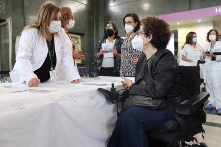 Una cuidadora se acerca a una mesa informativa (HOSPITAL VIRGEN DE LAS NIEVES) Una cuidadora se acerca a una mesa informativa (HOSPITAL VIRGEN DE LAS NIEVES)