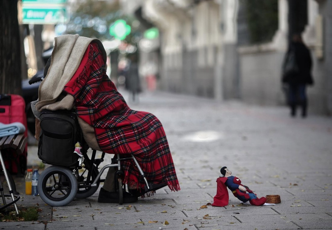 Una persona en silla de ruedas y tapada con una manta pide dinero con un muñeco de Superman (EDUARDO PARRA / EUROPA PRESS)